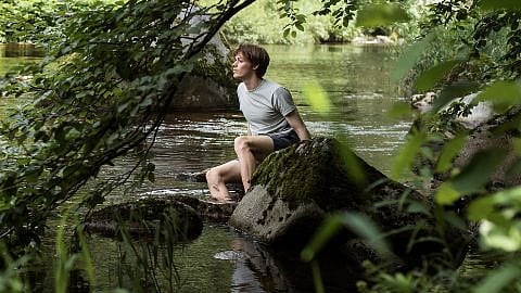 Mann sitter på en stein ved vannet.